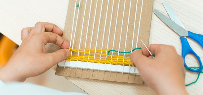 close up of hands weaving yarn on a cardboard loom