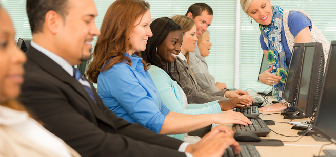 adults seated at computers with a teacher looking on
