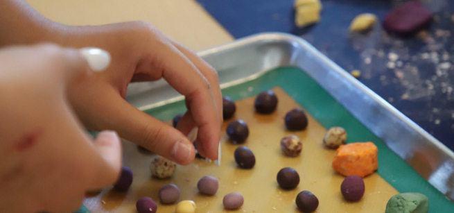 two hands reach for small balls of rolled rice dumplings on a baking sheet