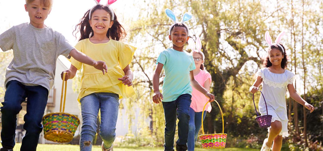 Group of children wearing bunny ears running to pick up Easter eggs during Easter egg hunt.