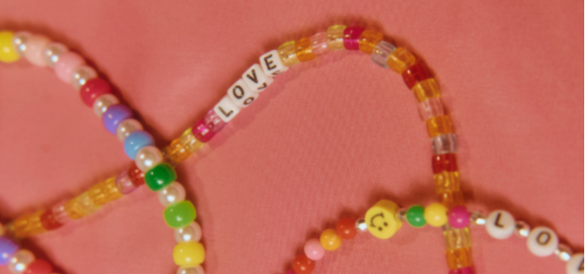 Three multicolored bead bracelets laid out on a pink background