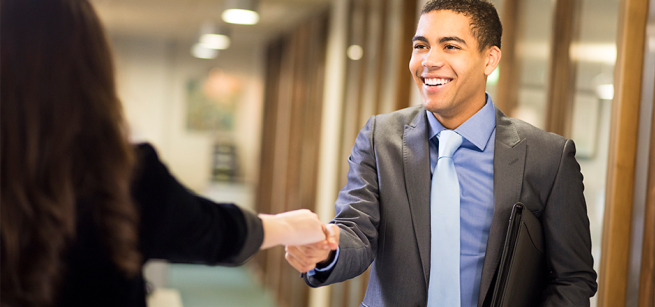 A young man in a suit and tie shaking hands with someone.