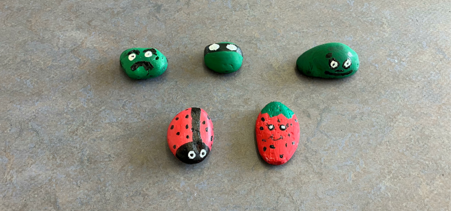 Five rocks painted to look like a ladybug, a strawberry, a ninja turtle and green monsters