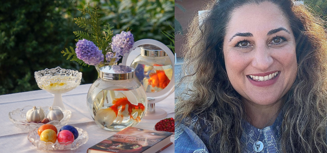 A portrait of presenter, Sanam Lamborn, next to a table decorated for Norouz with a goldfish bowl, a mirror, dyed eggs, and flowers.