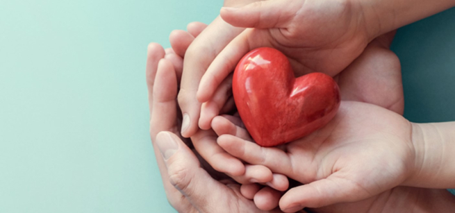 Multiple hands hold a painted heart sculpture.