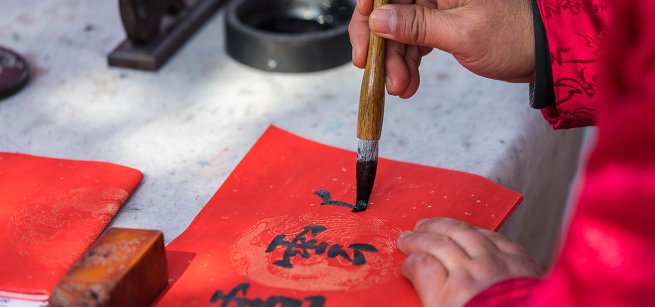Writing caligraphy on a paper with a bamboo brush.