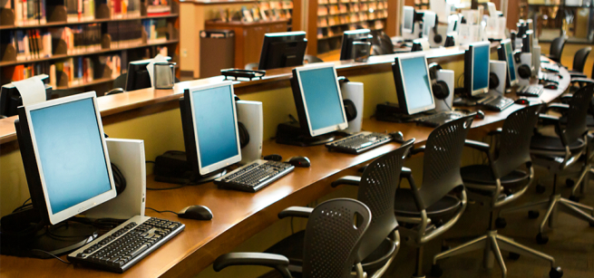 Long curved desk with row of computers inside a library.