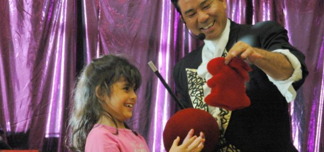 A male magician performing a magic trick with a young participant.