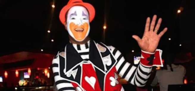 An adult clown waving his left hand.