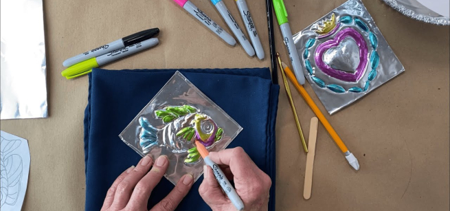 embossed fish and heart artwork colored with permanent markers by two human hands