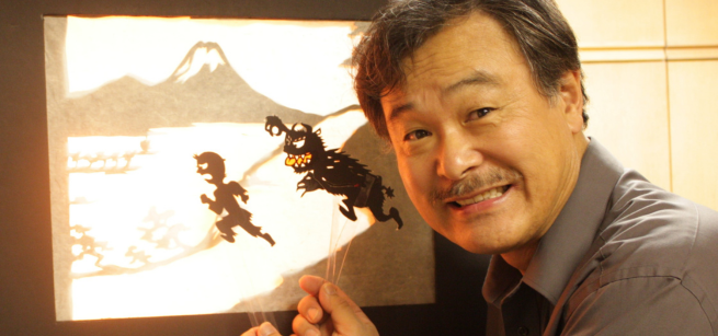 Sunny Seki holds shadow puppets against a projected screen.