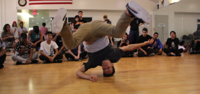 Guy breakdancing on a gym floor in front of spectators.