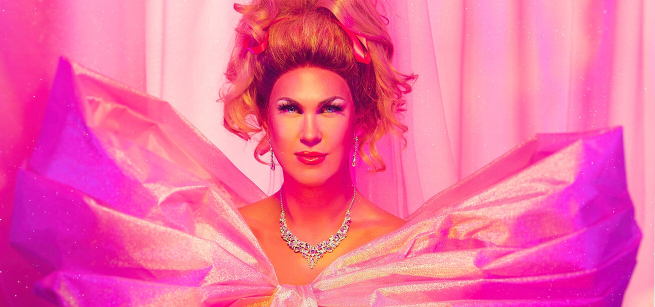 Head and shoulders view of Drag Performer Pickle in a pink gown, with a jeweled necklace and earrings, big hair, and full make-up.