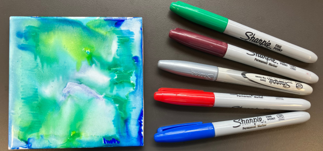 Five colored Sharpies to the right of a tie-dye tile coaster