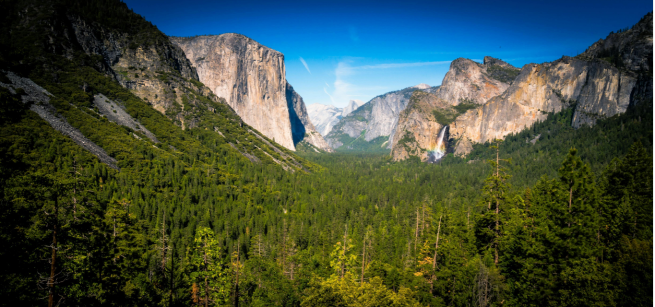 photo of Yosemite National Park, with green forest trees between a beige rock formation under a clear sky during daylight