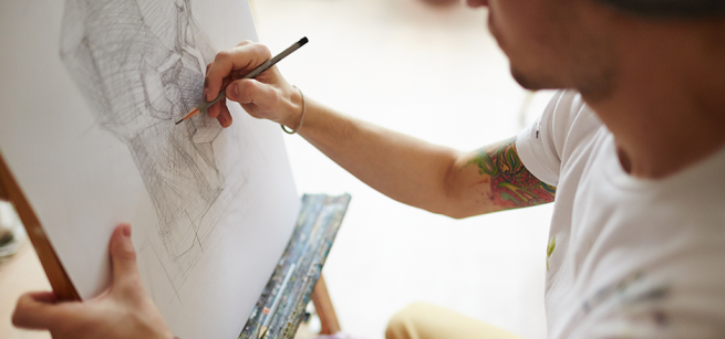 An artist draws with a pencil on paper supported by an easel.