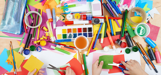 Paints, markers, and construction paper, with hands holding scissors cutting paper.