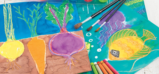 Watercolor paints and crayons are scattered around some artwork of fish and vegetables in the background. 