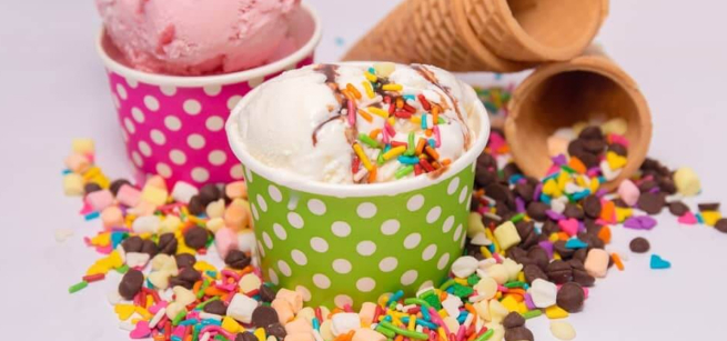Several cups of ice cream, cones, and many toppings