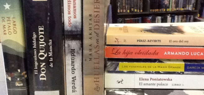 close up picture of 9 books in Spanish with bookshelves behind