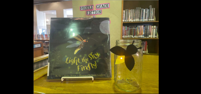 A sample light up firefly sits on a mason jar next to a copy of Light the Sky, Firefly!