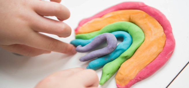 two hands arrange play dough into a rainbow shape