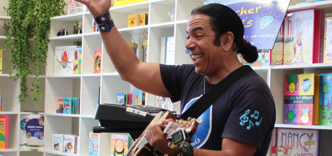 A smiling man holds a guitar