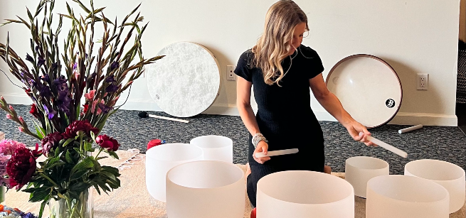 A woman in a black dress performs using seven quartz bowls laid out in front of her