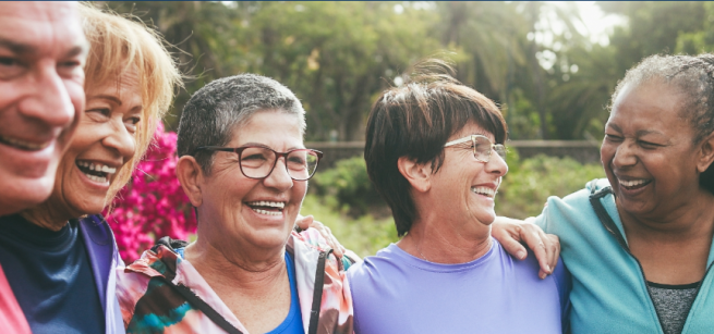 Five smiling adults walking in a park.