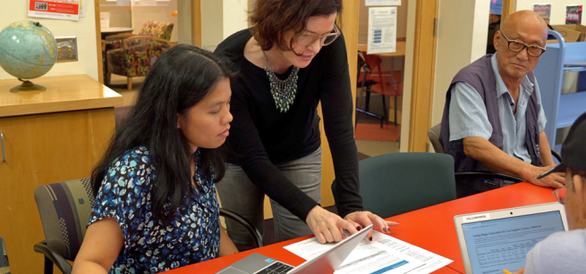 Adults getting help from a volunteer tutor at the library.