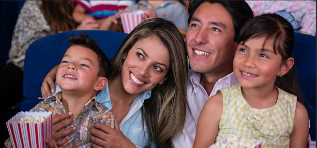 Family of four smiling in a movie theater watching a film