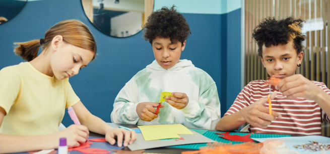3 kids sitting at table and cutting paper