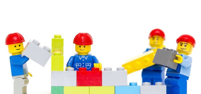 4 LEGO mini figures holding LEGO bricks. 