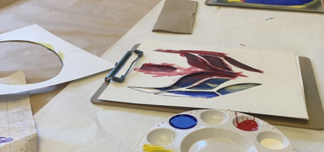 a stencil of a lucha libre mask on a table with paper and a palatte of paint colors nearby