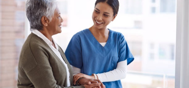 older adult dressed in a brown sweater walking with nurse