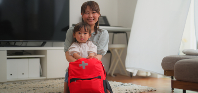 Daughter is sitting on the lap of her mother and holding a safety red cross signed ba