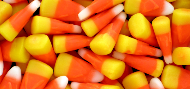 Bright, colorful candy corn pieces fill the image. Each piece has a yellow base, orange middle, and white tip, conveying a festive Halloween vibe.