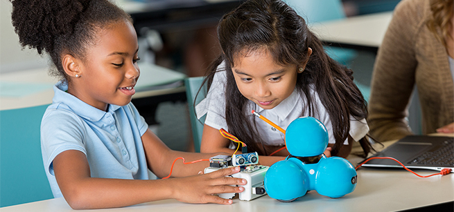 Two girls looking at a small mechanical experiment.