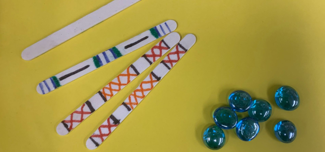 Four popsicle sticks with multicolored designs on them and a cluster of blue marbles. 