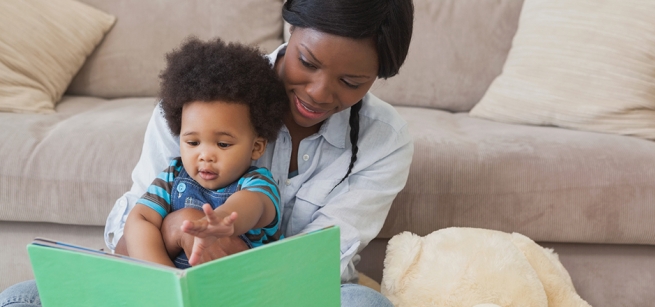 A mother reads from a book to the baby sitting in her lap.