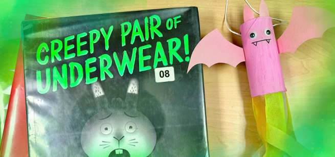 A pink bat craft with tissue paper is displayed beside spooky children's picture books.