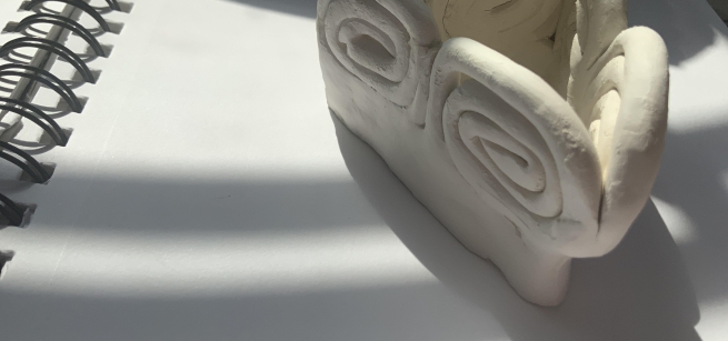 A clay sculpture with swirls on top of a sketchbook. 
