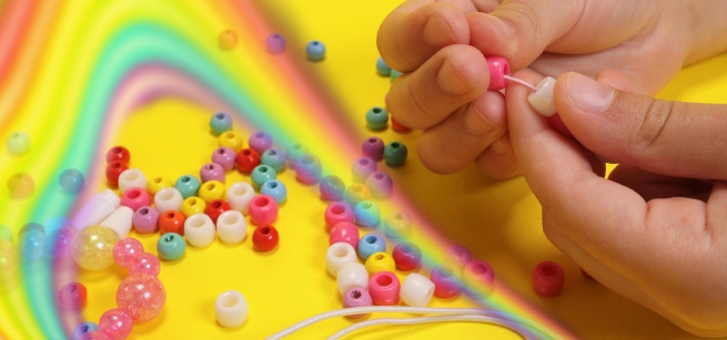 A hand stringing beads on a yellow background with a rainbow