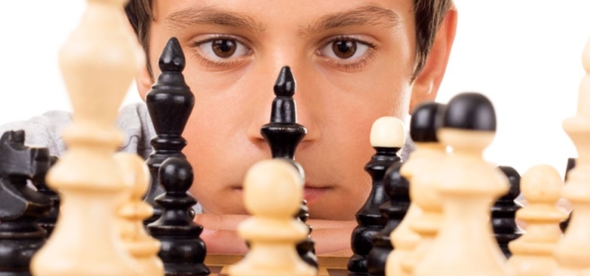 Young boy looking at chess pieces.