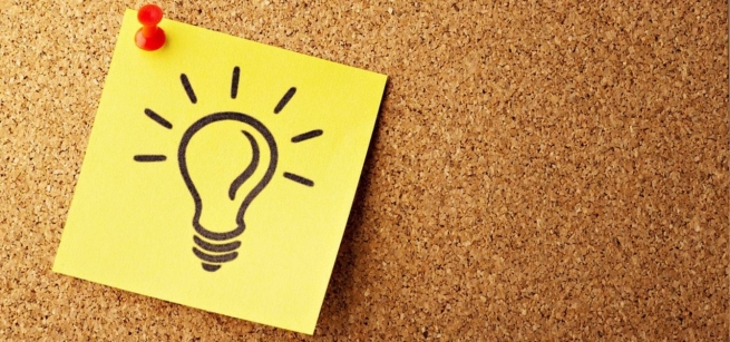 a post-it note with a lightbulb drawn on it is thumb tacked to a corkboard