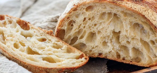 image of a loaf of sourdough bread with one slice cut off on a tan cloth on a cutting board.