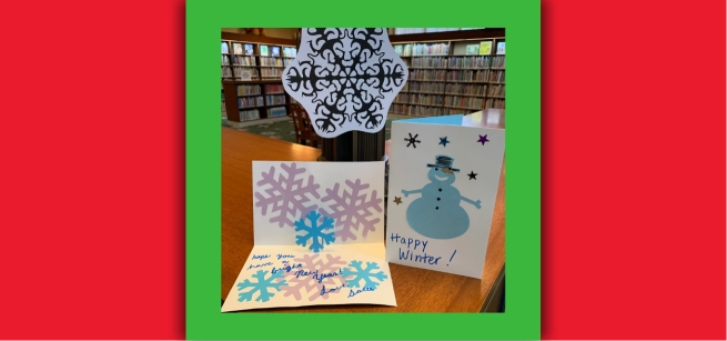A paper snowflake and two paper greeting cards with images of snowflakes and a snowman.