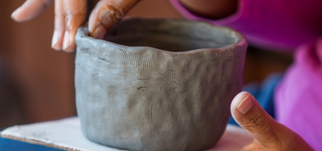 fingers shaping a small gray clay pot