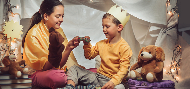 Two children engage in a tea party inside of a blanket fort