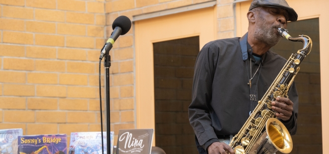 Cyril Carr playing the sax in the Watts library courtyard with jazz picture books in the background